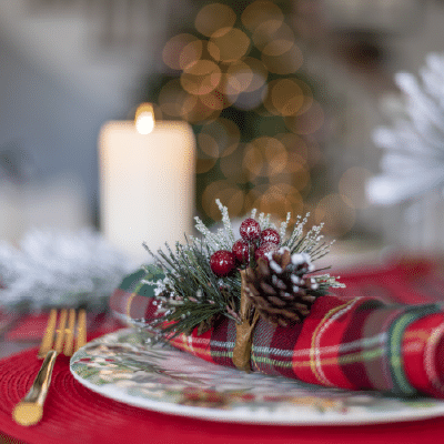 Dec 8, Christmas Holiday Luncheon: Holiday place setting with a plaid napkin, pinecone and berry sprig, and a lit candle.